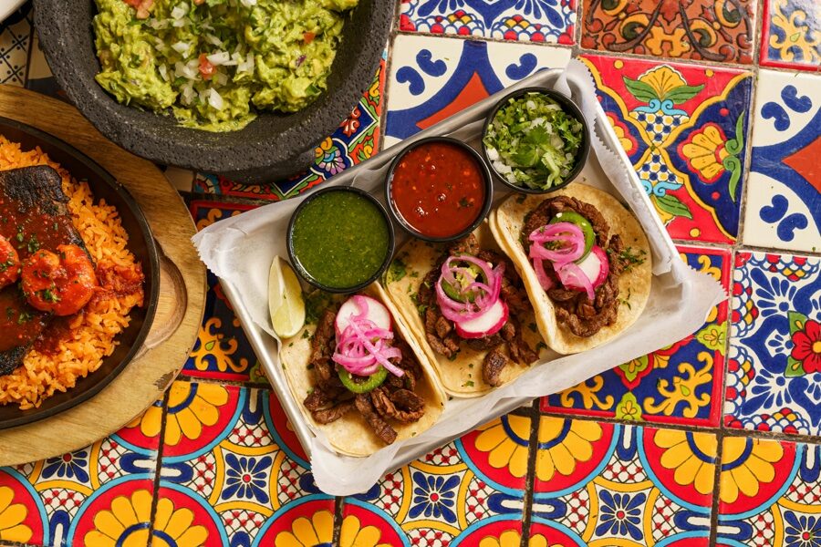 Festín de tacos callejeros con salsas roja y verde sobre azulejos de talavera